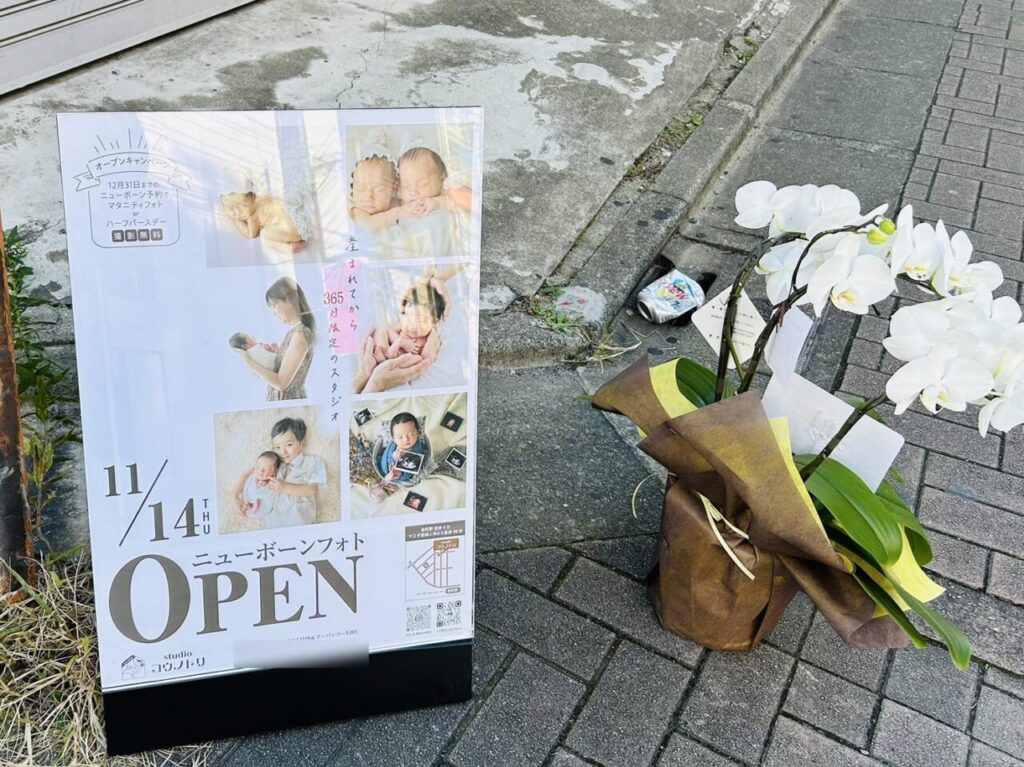 道端に置かれた開店祝いの花とOPENのポスター
